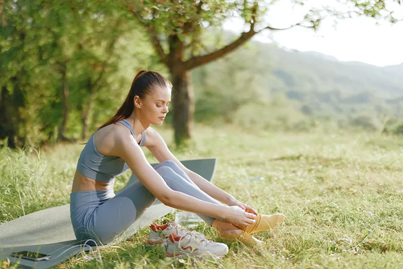 Young woman practicing yoga outdoors in activewear, embodying relaxation and focus, surrounded by lush greenery in a serene natural setting