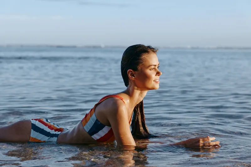 Woman in ocean water, swimming near beach, fitness and summer wellness, outdoors calm moment, side view in sea, waves and sunlight, focused athlete relaxing, natural health and hydration