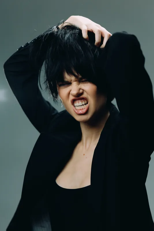 angry woman with black hair and intense expression in dark outfit showing frustration