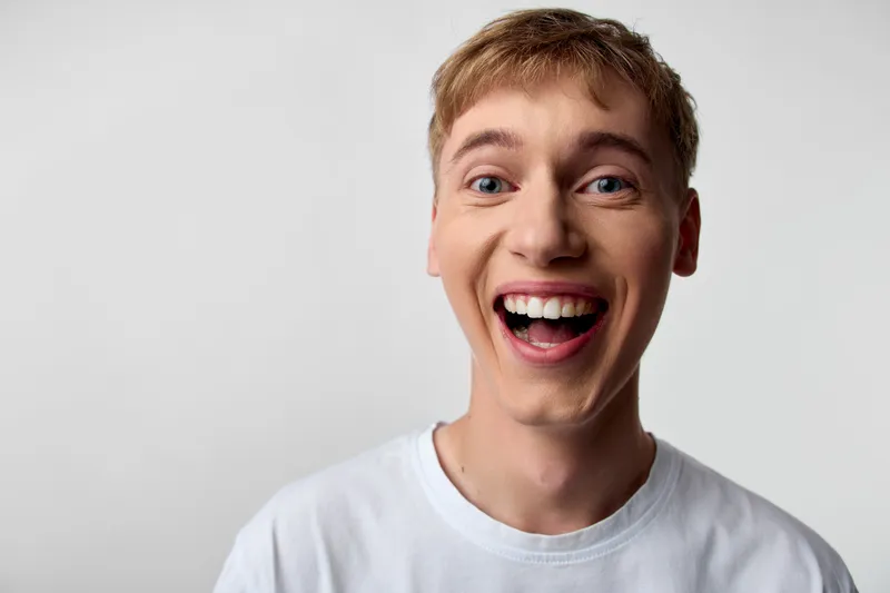 Closeup of an excited man with a wide smile, wearing a white tee, in a studio, expressing happiness and energy for lifestyle, advertising and promotional use