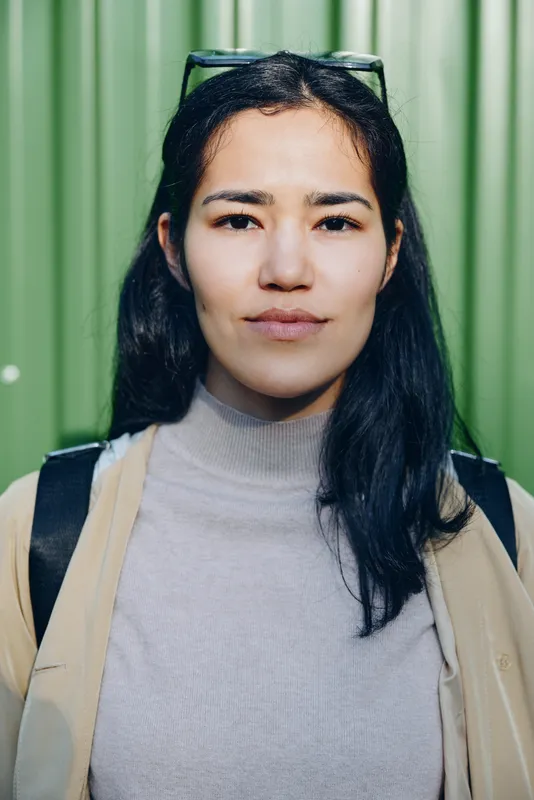 Woman, backpack, outdoors, green, casual expression and lifestyle travel scene with natural light, wearing simple jacket, conveying everyday readiness for urban exploration and street style