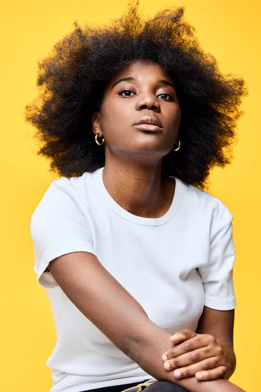 Portrait of a confident young Black woman with natural afro hairstyle against a bright yellow background, showcasing beauty and self expression in a minimalistic style