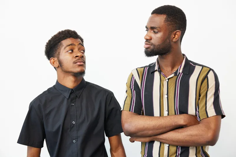 Black men engaging in a friendly conversation, showcasing emotions of joy and camaraderie. The warm colors and relaxed attire create a welcoming atmosphere.