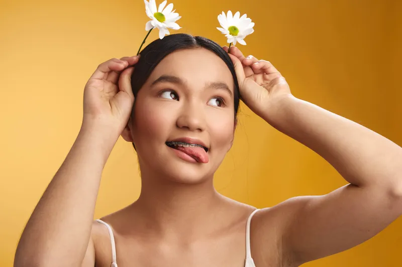 asian woman with flowers in her hair playfully poses against a warm backdrop, creating a light, joyful mood that conveys creativity and spontaneity in a friendly setting.