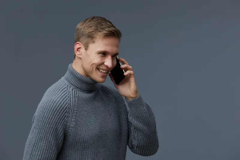 smiling man talking phone wearing gray knitted sweater looking aside communication cyber security concept