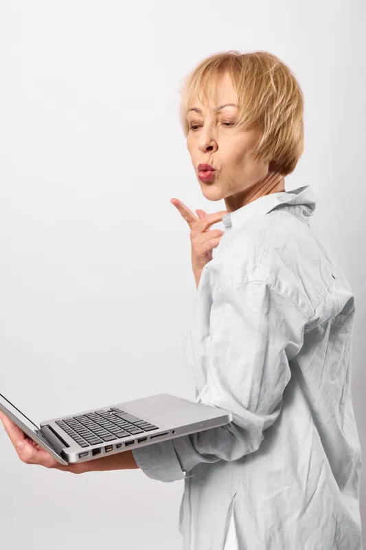 Woman laptop communication business office technology studio portrait mature employee in white blouse holds a laptop and gestures while speaking in a minimal studio