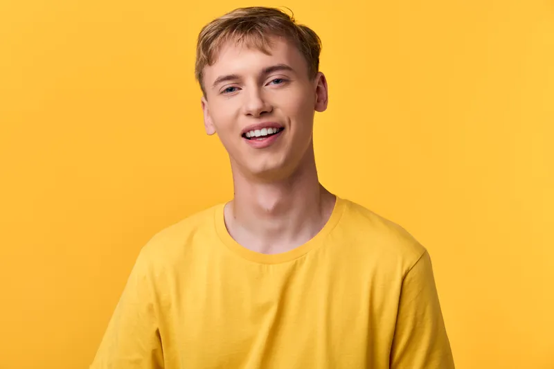 Close up of a smiling man in a bright yellow shirt against a warm backdrop, conveying optimism, friendliness and casual style for lifestyle, marketing and positive messaging in stock photography.