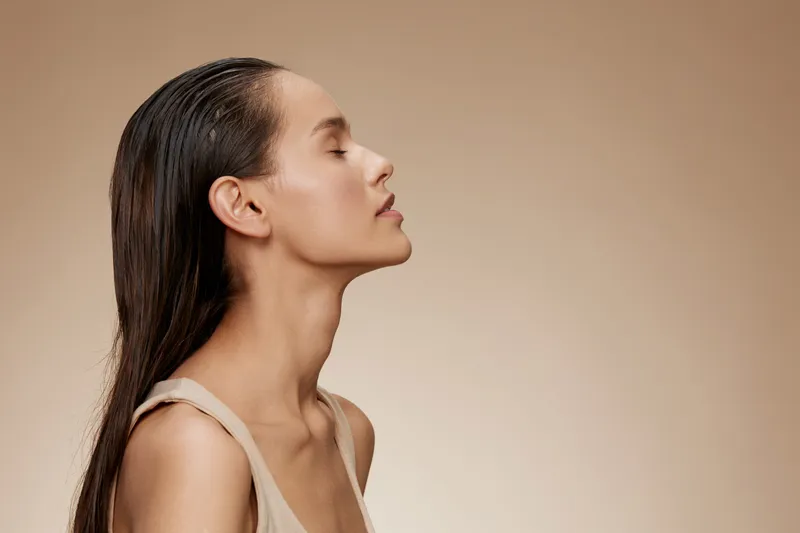 Serene female model with long wet hair, eyes closed, on a soft beige background, expressing calmness and beauty in a minimalist fashion