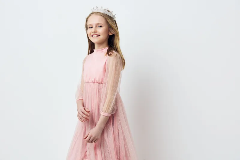 Young girl in a pink dress smiling, wearing a floral crown, light and airy background, conveying joy and innocence, perfect for children s fashion and spring themes