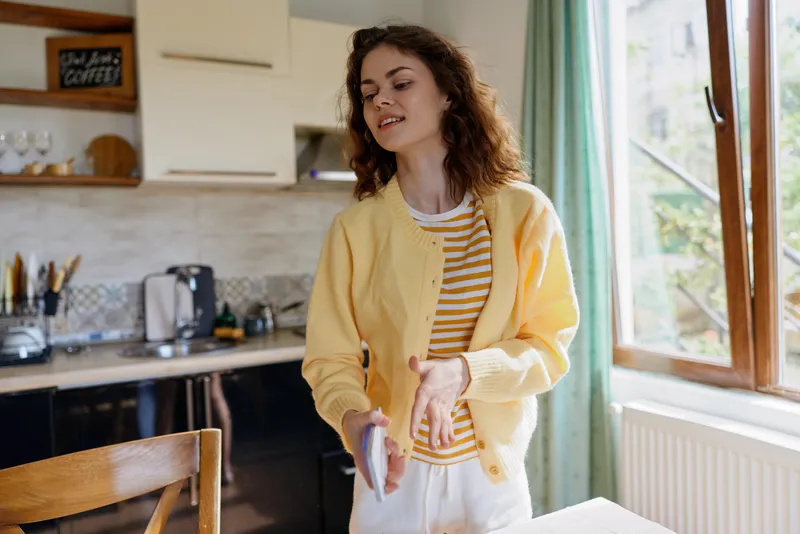 Smiling woman in a yellow cardigan cooking in a bright kitchen at home, capturing a casual lifestyle moment with warm natural light, soft textures, and inviting, cozy decor.