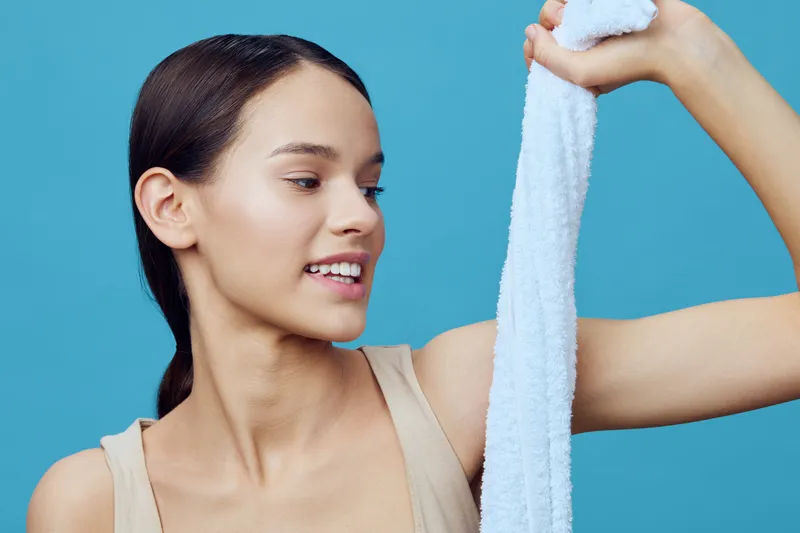 Young woman enjoying healthy skincare routine with towel on blue background, showcasing natural beauty and wellness