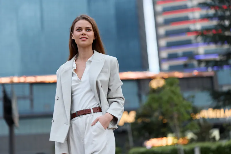 confident woman in beige business suit outdoors smiling with modern urban background, professional, stylish, positive mood, business concept