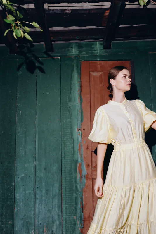 woman in yellow dress portrait by rustic wooden wall, vintage style, natural light, authenticity inclusivity, thoughtful pose and soft shadows for fashion lifestyle