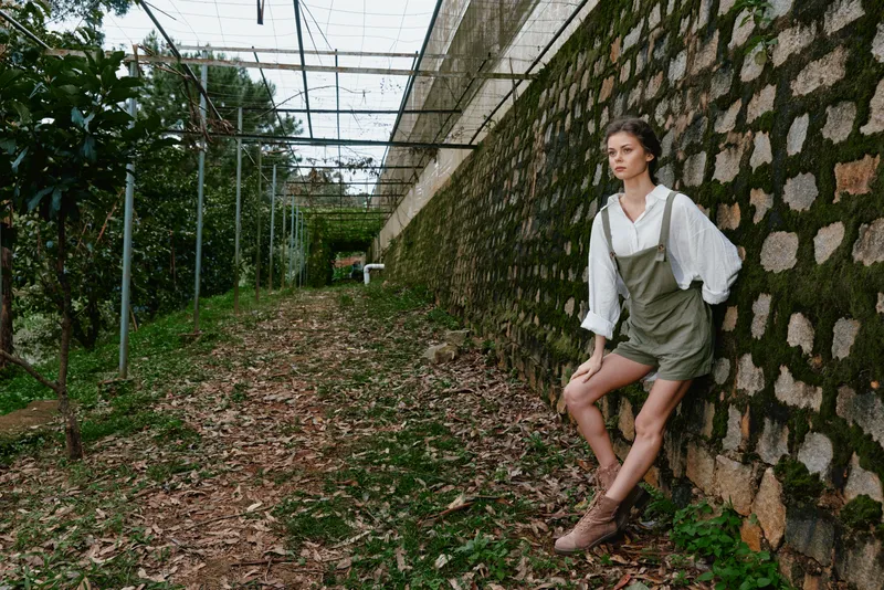 Young woman in casual attire leaning against a stone wall in an outdoor setting, capturing a moment of serenity surrounded by nature