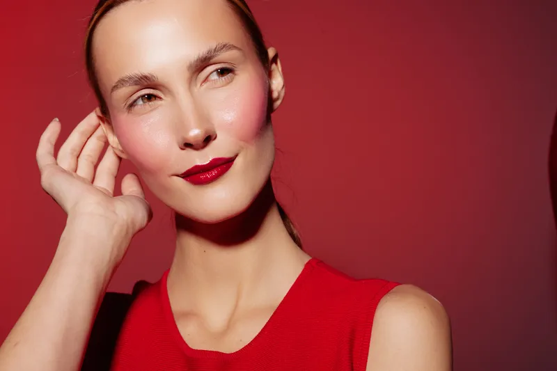 Portrait of a confident woman with red lipstick and blush wearing a red sleeveless top on red background. Concept of beauty, makeup, fashion, and elegance.
