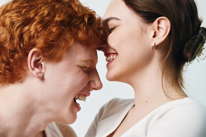 Young couple with close faces laughing and enjoying tender moment, smiling woman and man with red hair in casual clothes on white background expressing happiness and love.