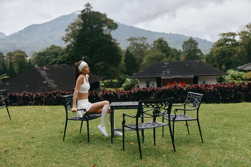 Young woman in sporty outfit enjoying nature in a serene garden, exuding calmness and peace against a picturesque mountain backdrop