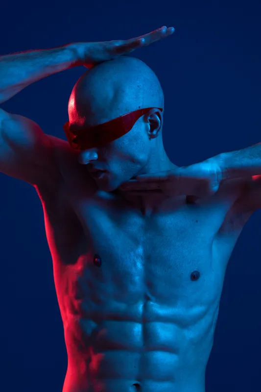 Athletic man posing with stylish sunglasses against a vibrant blue background, showcasing modern aesthetics and dynamic lighting. A striking color image with energy.