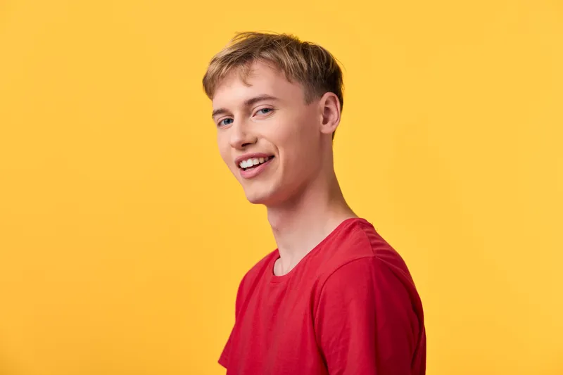 Smiling man in a red shirt stands against a bright yellow background, conveying casual style, optimism and youthful energy, ideal for lifestyle, fashion or positive message campaigns