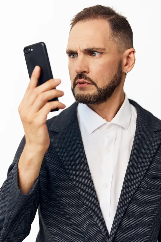 Professional man in a blazer studies a mobile device, conveying focus and determination. Solid color background highlights a confident, thoughtful business persona.