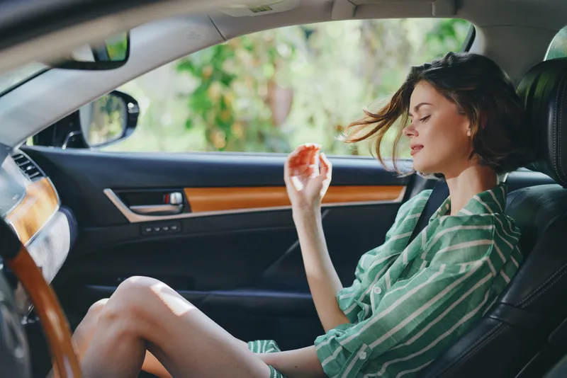 Young woman enjoying a snack inside a stylish car, seated comfortably with a relaxed pose, wearing a green striped shirt, natural light creating a calm moment.