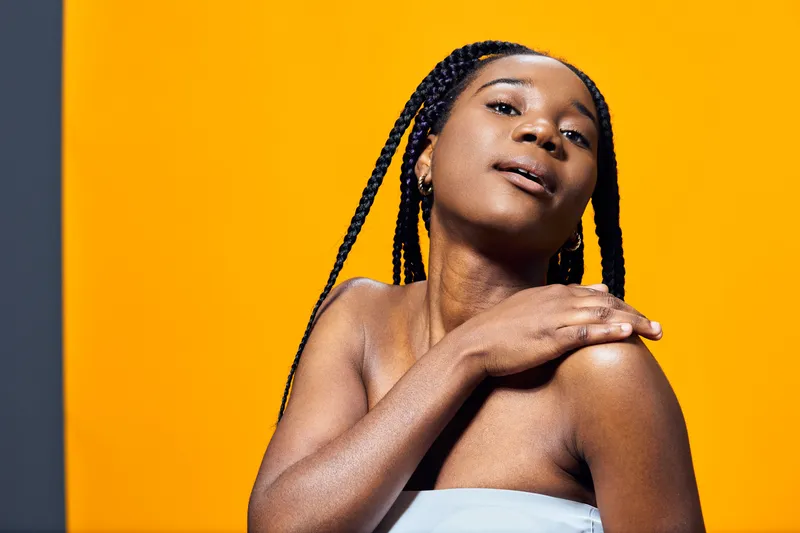 Portrait of a young Black woman with braids against a vibrant yellow background, showcasing confidence and self expression through fashion and emotion