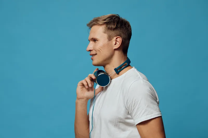 Profile side view smiling young caucasian man wear white t-shirt hold wireless headphones looking ahead isolated on blue background digital detox concept