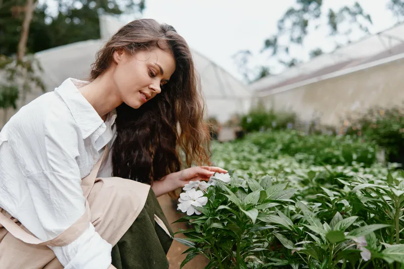 Beautiful young woman appreciating flowers in a green garden, showcasing a serene emotion and natural springtime vibes with a soft color palette