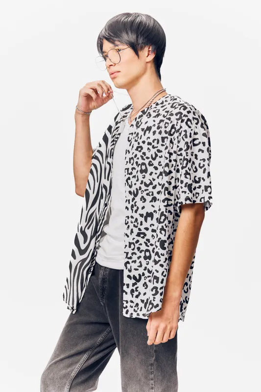 young man wearing trendy animal print shirt and glasses, posing thoughtfully against a plain white background, stylish casual outfit with monochrome palette.