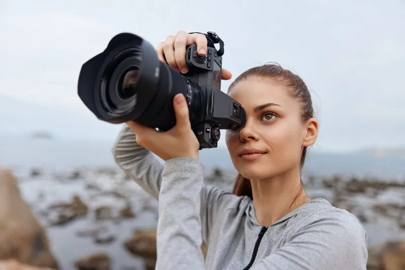 Young woman photographing with a DSLR camera by the seaside, showcasing passion for photography and adventure