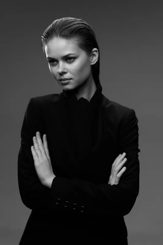 Black and white portrait of serious woman with crossed arms wearing dark jacket against plain background.