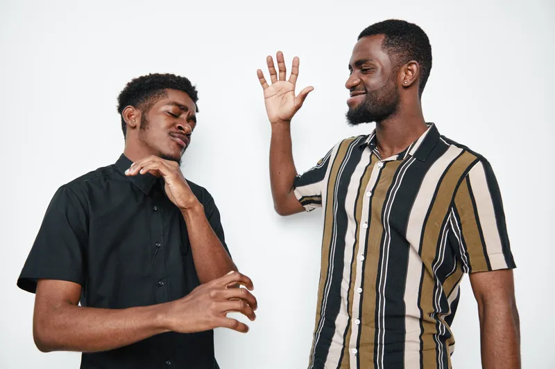 Two young black men with dark skin playing and smiling together in casual clothes on white background. Friends having fun and enjoying positive interaction indoors.