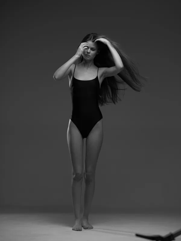 slender woman in black swimsuit adjusting hair, black and white, studio portrait, graceful pose
