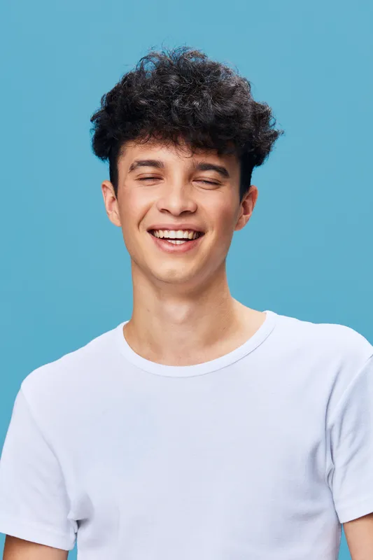 smiling man with curly hair wearing white t-shirt against blue background, joyful expression, youthful, casual style, positive mood