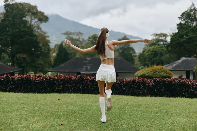 Young woman in sporty attire running joyfully in a green park surrounded by mountains, expressing happiness and freedom in a vibrant outdoor setting
