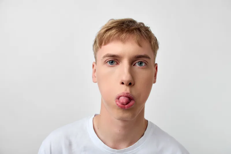 Tongue out playful expression on a young man wearing a white t shirt, close up shot in studio light, candid mood, casual style with an energetic vibe and expressive face