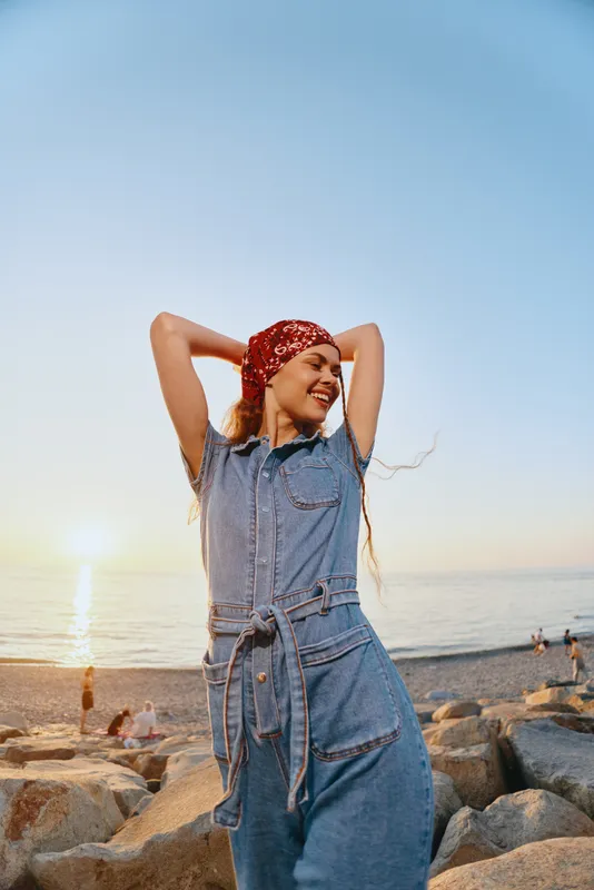 lifestyle woman in modern boho-western denim street style smiling with red bandana near beach at sunset with warm film color tones and relaxed mood