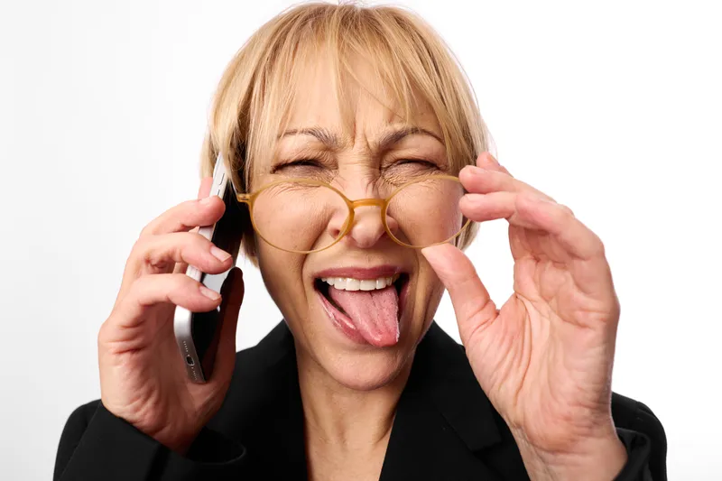 Playful woman adjusting glasses with hands, tongue out in a funny expression, closeup portrait in studio lighting, on white background, eyewear and face gesture, comedy mood