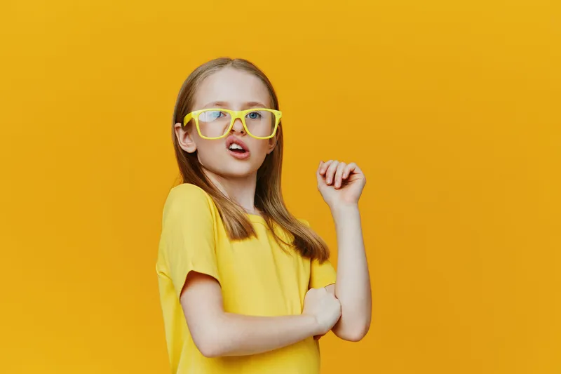 A cheerful Caucasian girl posing confidently in stylish yellow glasses and a matching t shirt against a vibrant yellow background, showcasing summer fun and youthful style