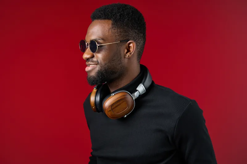 Stylish young Black man wearing sunglasses and headphones on a red background, exuding confidence and modernity in a fashionable outfit