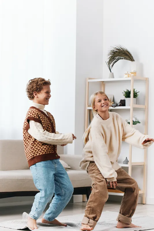 Authenticity shines as two children laugh and dance at home, capturing a playful moment that emphasizes a wholesome lifestyle and the spirit of school life in everyday play.