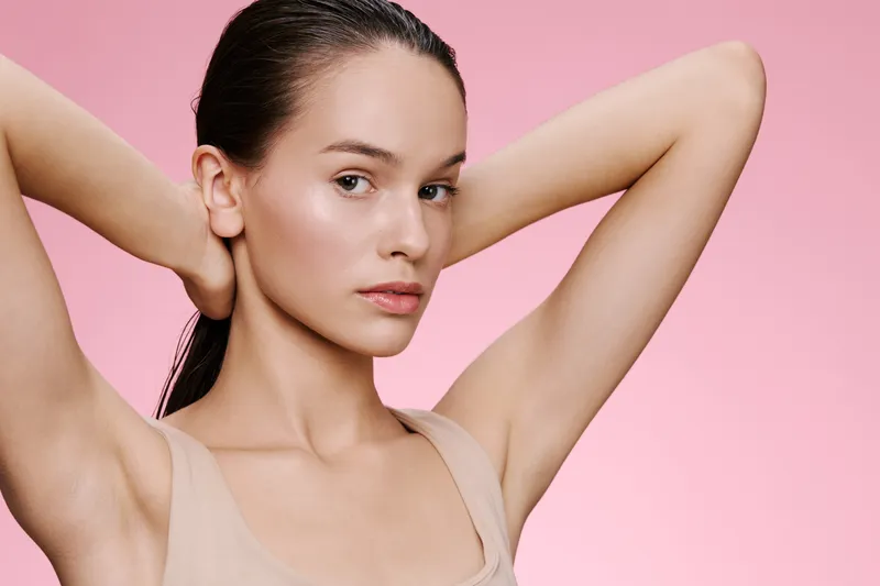 Young woman with sleek hair against a light pink background, conveying confidence and beauty in a minimalist aesthetic with natural makeup