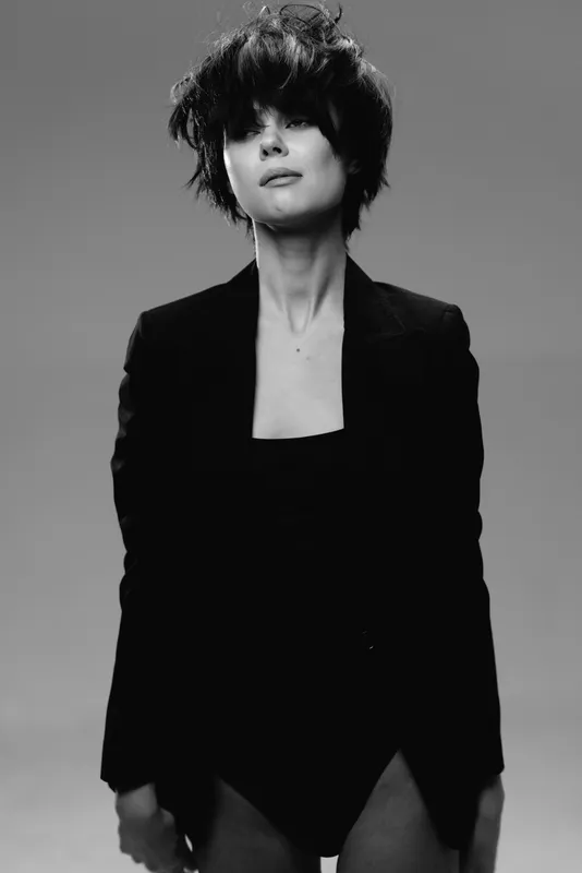 Black and white portrait of a confident woman with curly hair wearing a blazer in studio lighting.