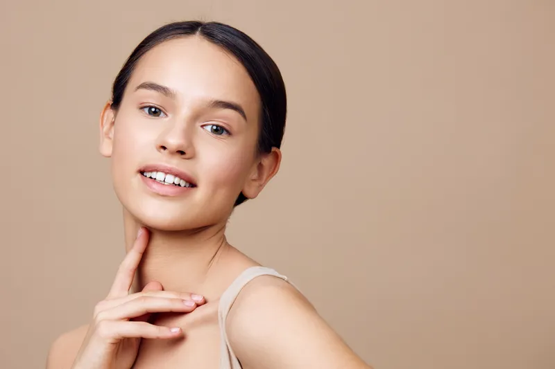 Young woman with a charming smile and natural beauty, wearing minimal makeup, against a beige background, perfect for beauty and skincare concepts