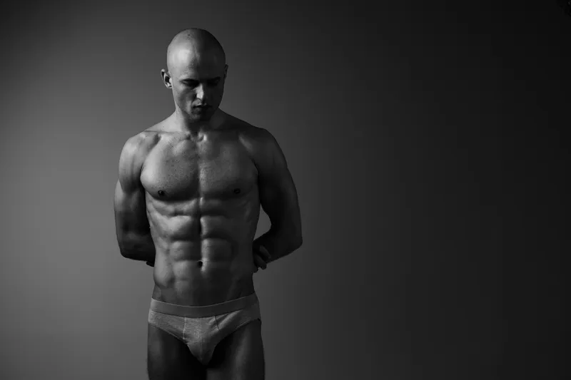 Muscular man in black and white, showcasing strong physique and intense expression, stands against a neutral background, embodying strength and determination.
