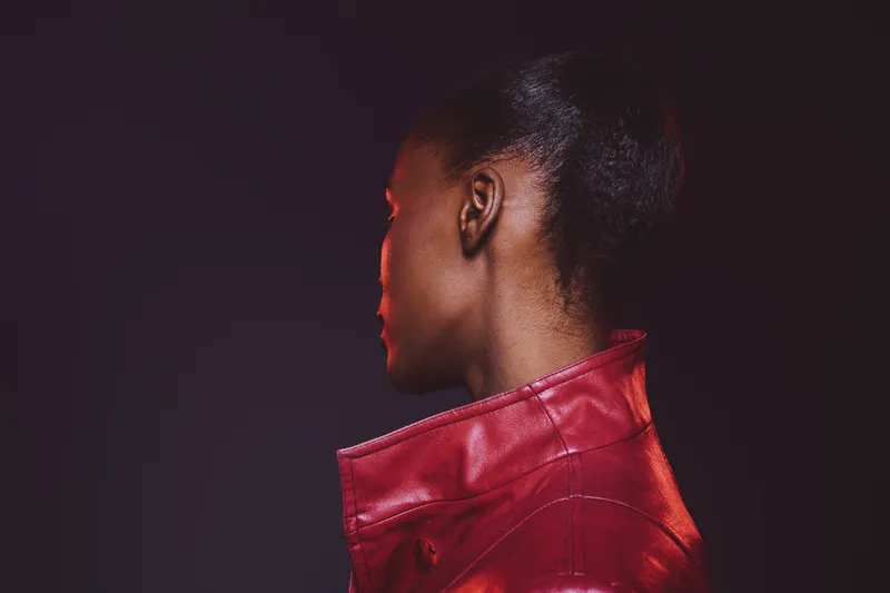 Profile of a young black woman with dark skin wearing a red leather jacket against a dark background. Concept for fashion, portrait, and modern style with moody lighting.
