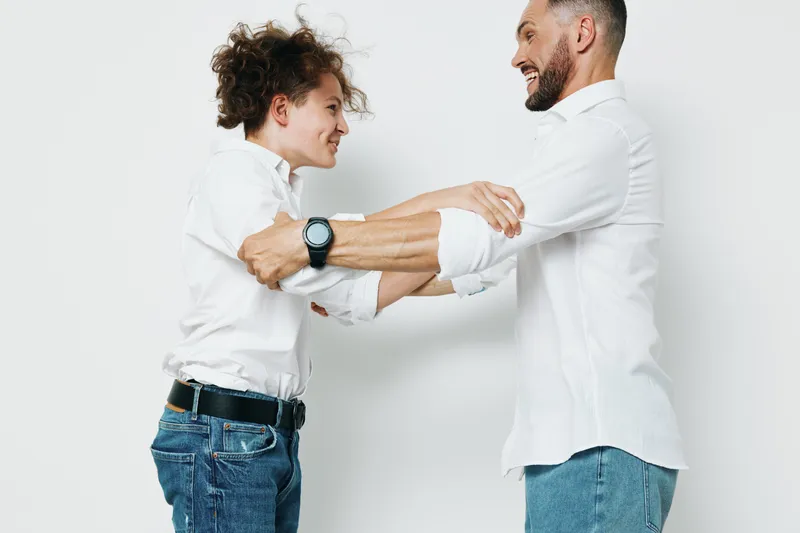 Professional man and colleague on a solid colored backdrop, showing warm emotions and teamwork during a friendly business moment in a modern setting.