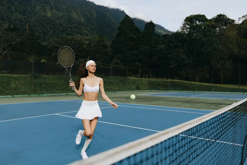 A joyful female tennis player enjoying a sunny day on the court, wearing a white sports outfit, capturing the essence of athleticism and enthusiasm