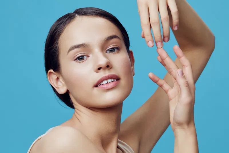 Young woman with a serene expression, showcasing elegant hand poses against a bright blue background, emphasizing beauty and femininity in a minimalist style
