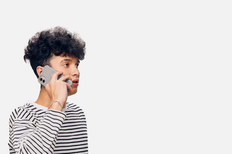 Young man talking on smartphone wearing a striped shirt, isolated on white background, casual style, communication concept.